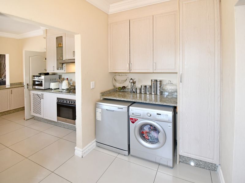 A functional scullery area featuring built-in cabinetry, granite countertops, and tiled flooring, with an adjacent kitchen visible through the doorway.
