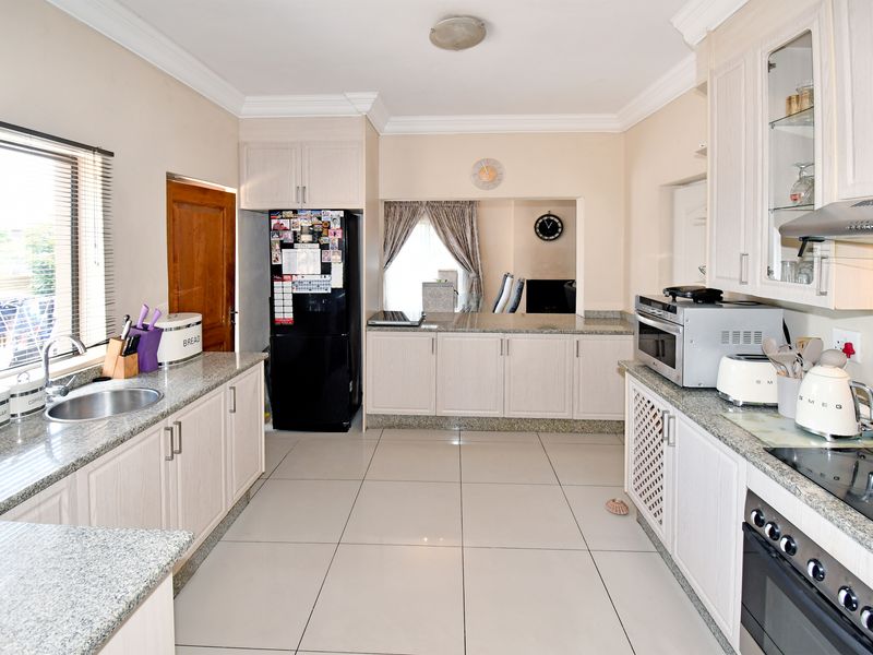 A functional kitchen featuring granite countertops, ample built-in cabinetry, ceramic floor tiles, and integrated cooking appliances including an oven and hob.