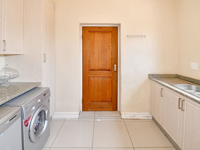 A functional laundry room featuring built-in cabinetry, granite countertops, a stainless steel double sink, and tiled flooring with a timber door.