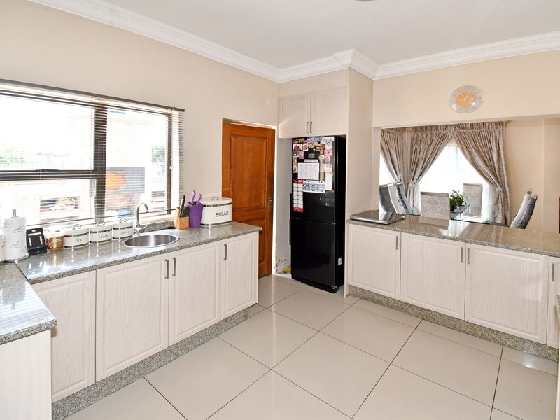 Functional kitchen featuring granite countertops, light wood-finish cabinetry, tiled flooring, and a convenient breakfast bar pass-through to the adjacent living area.