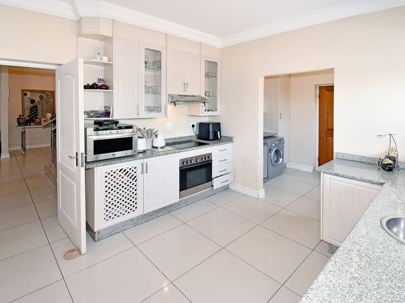 A functional kitchen featuring light wood-finish cabinetry, granite countertops, integrated oven and hob, and tiled flooring, with an adjacent laundry area.