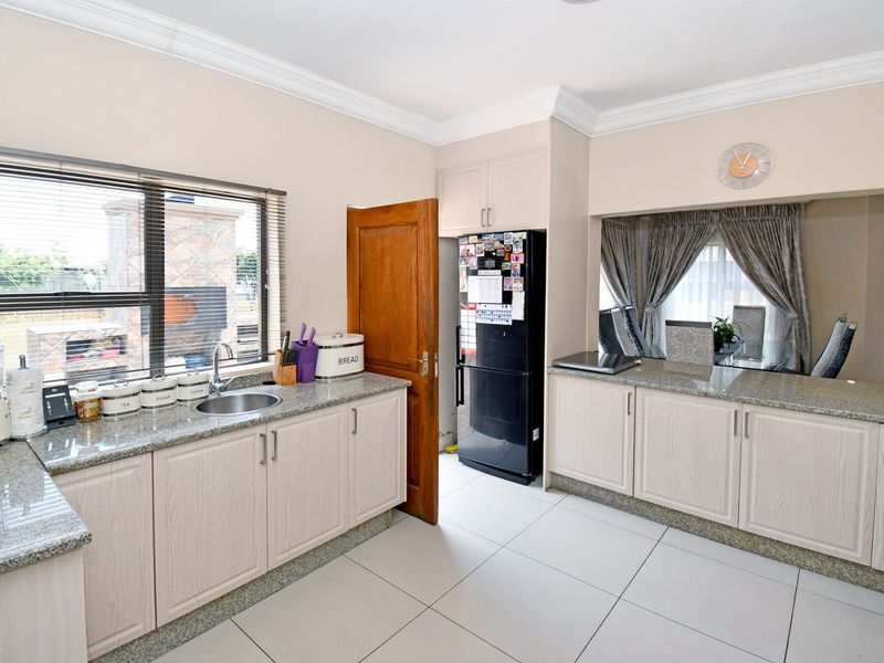 A functional kitchen featuring granite countertops, light wood-finish cabinetry, tiled flooring, and a convenient serving hatch connecting to the dining area.