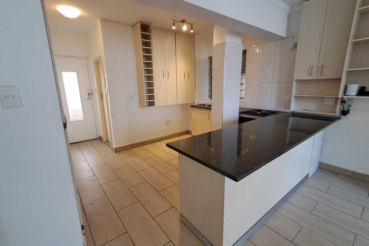 Open-plan kitchen featuring granite countertops, built-in cabinetry, a breakfast bar, and ceramic floor tiles, offering a functional layout for modern living.