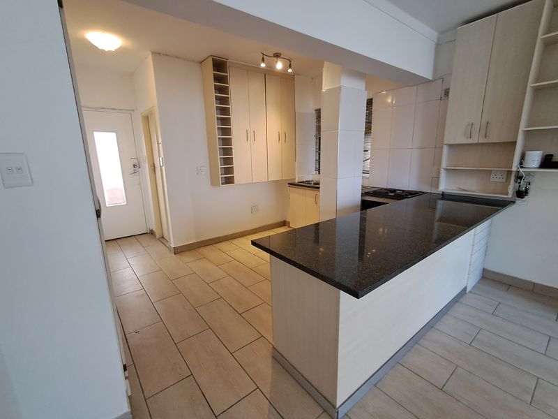 Open-plan kitchen featuring granite countertops, built-in cabinetry, a breakfast bar, and ceramic floor tiles, offering a functional layout for modern living.