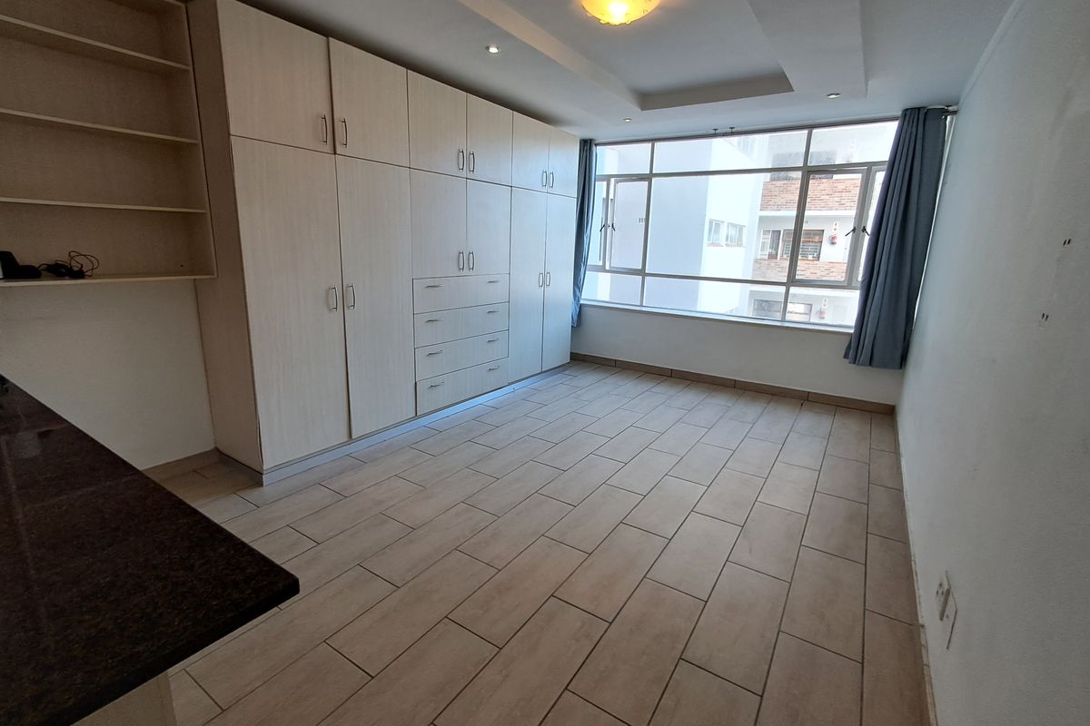 A bright, empty bedroom featuring extensive built-in cabinetry, modern tiled flooring, and large windows providing natural light.