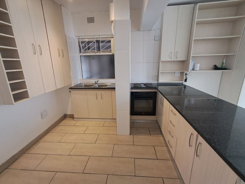 A functional kitchen featuring light wood cabinetry, dark granite countertops, built-in oven and hob, and tiled flooring.