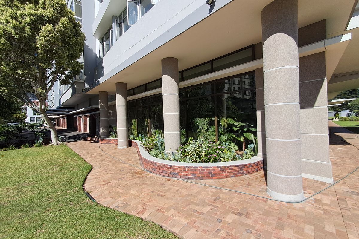 A well-maintained exterior rear area featuring a brick paved walkway, curved brick planter box, and concrete support columns along the apartment building facade.
