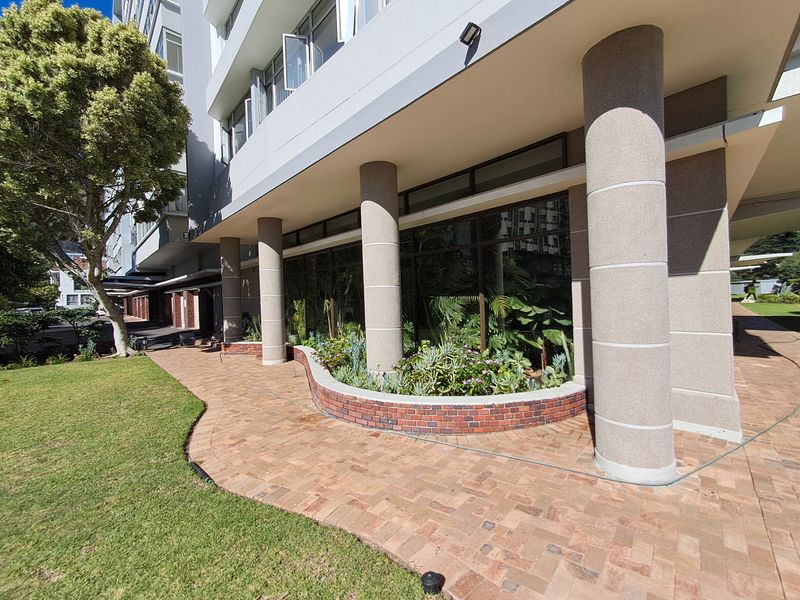 A well-maintained exterior rear area featuring a brick paved walkway, curved brick planter box, and concrete support columns along the apartment building facade.