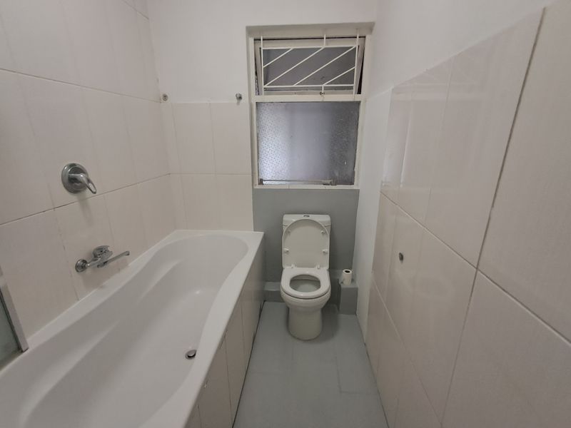 A compact bathroom featuring a standard bathtub, toilet, and tiled walls. The space is functional but would benefit from cosmetic updates.