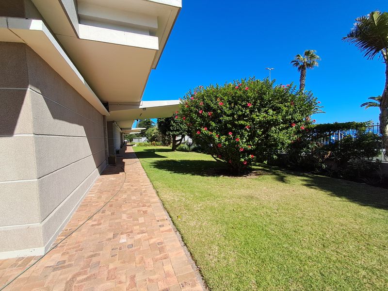 A well-maintained rear exterior area featuring a brick paved walkway alongside a landscaped garden with mature shrubs and overhanging roof eaves.