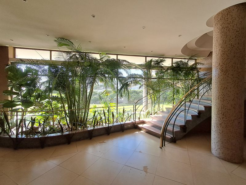 Spacious entrance foyer featuring a striking mosaic-tiled column, a curved staircase with a metal handrail, and large windows overlooking the garden.