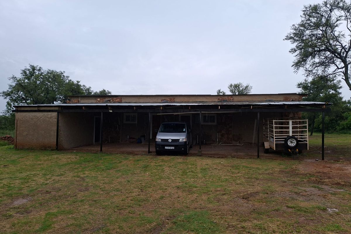 A single-story structure featuring a covered outdoor area with exposed brickwork and metal roofing, set on a large open plot.