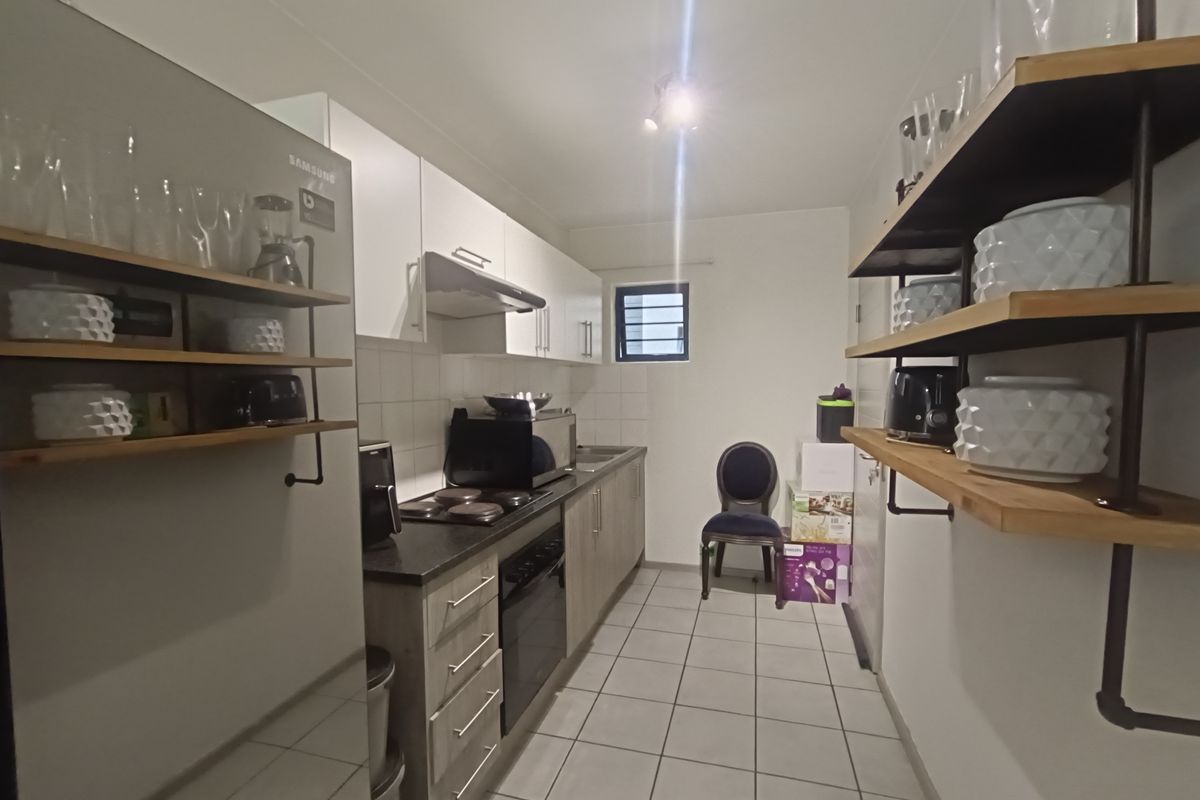 A functional galley-style kitchen featuring built-in cabinetry, a hob, an oven, an extractor fan, and open shelving with tiled flooring throughout.