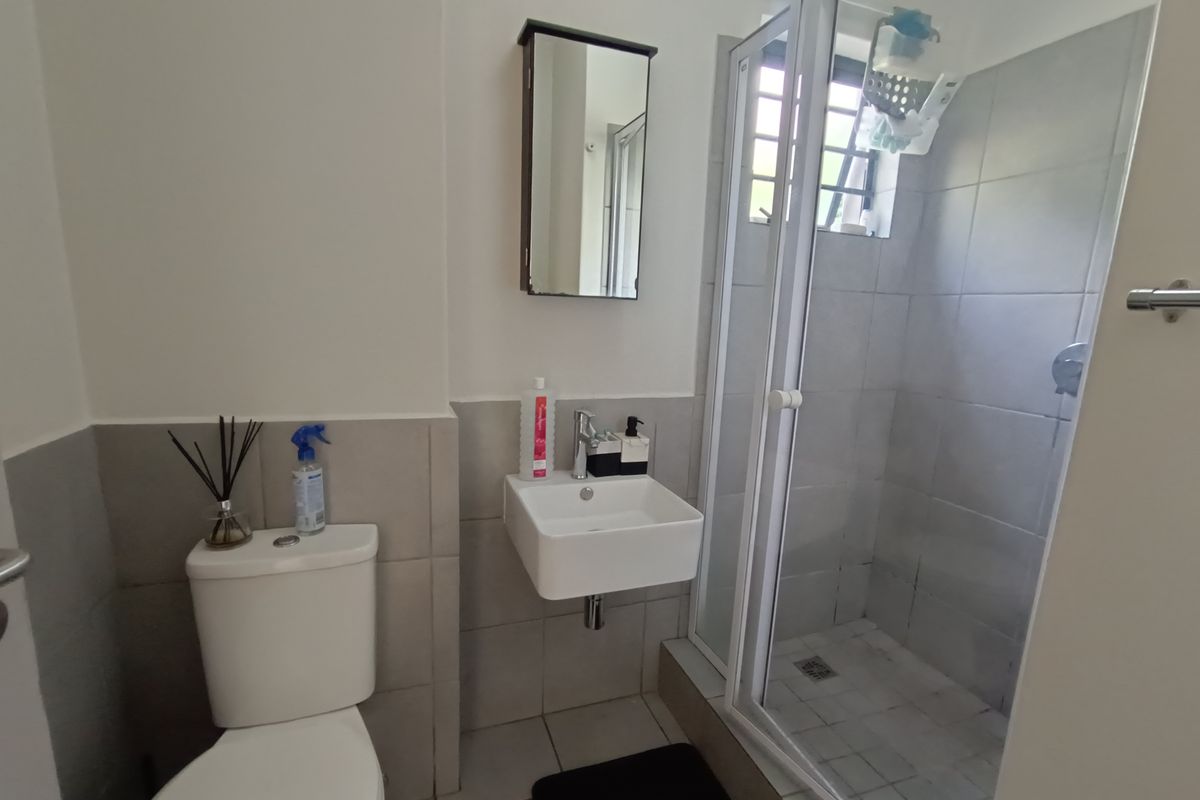 A compact bathroom featuring a wall-mounted basin, a shower enclosure with glass doors, and a standard toilet with neutral wall and floor tiling.