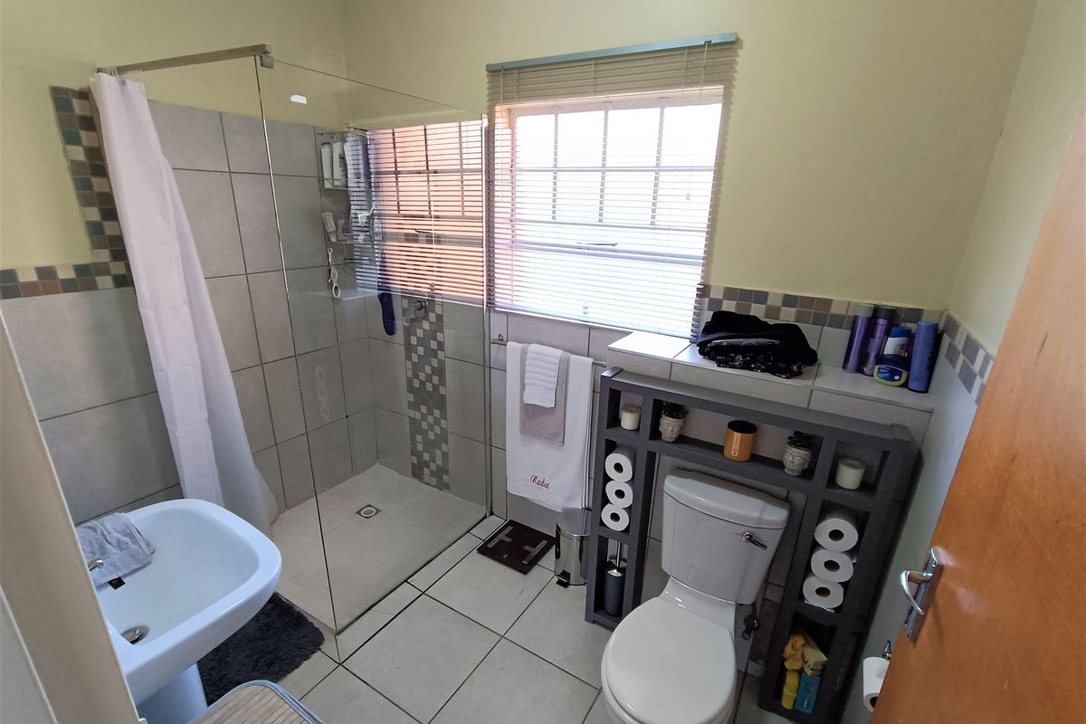 A functional bathroom featuring a glass-enclosed shower, pedestal basin, toilet, and neutral tiled finishes with decorative accent borders.