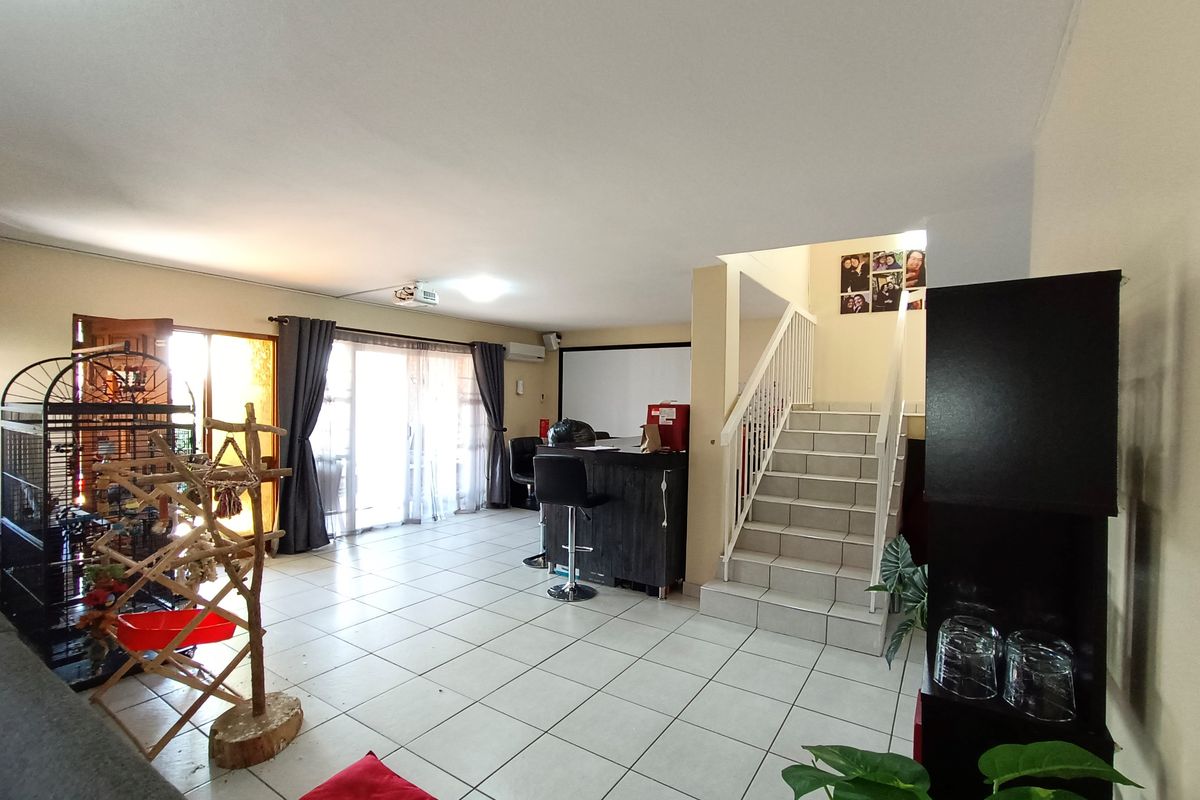 Spacious open-plan living area featuring tiled flooring, a staircase with a metal balustrade, and sliding glass doors leading to the exterior.
