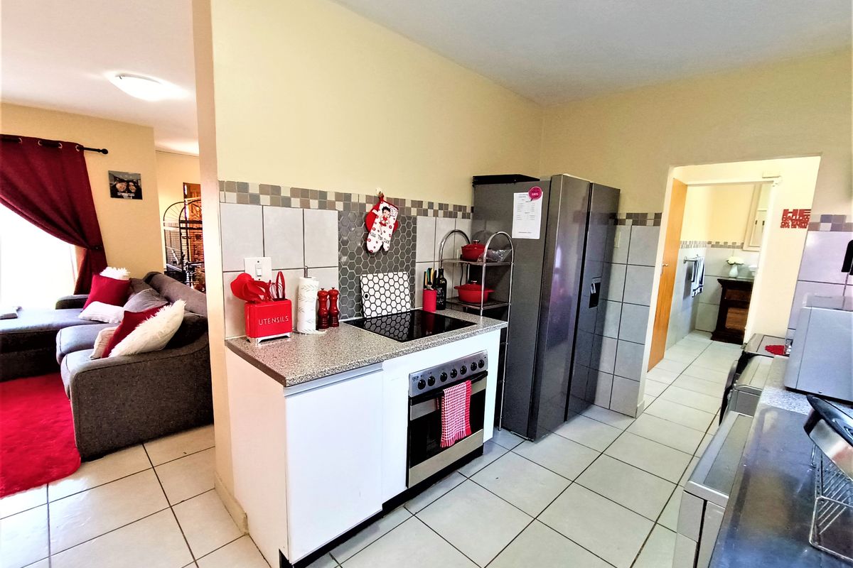 A functional kitchen featuring a built-in oven, electric hob, tiled splashback, and ceramic floor tiles, seamlessly connected to the adjacent living area.