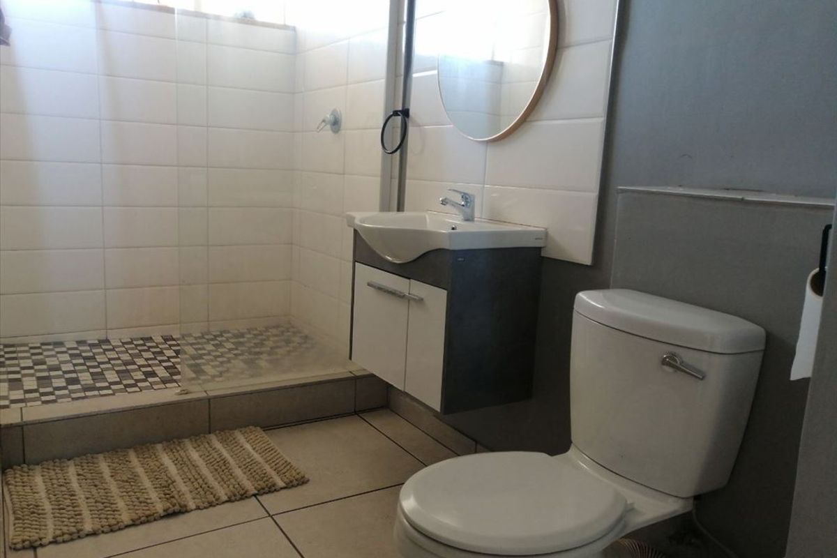 A modern bathroom featuring a walk-in shower with mosaic floor tiles, a wall-mounted vanity with basin, and a standard toilet.