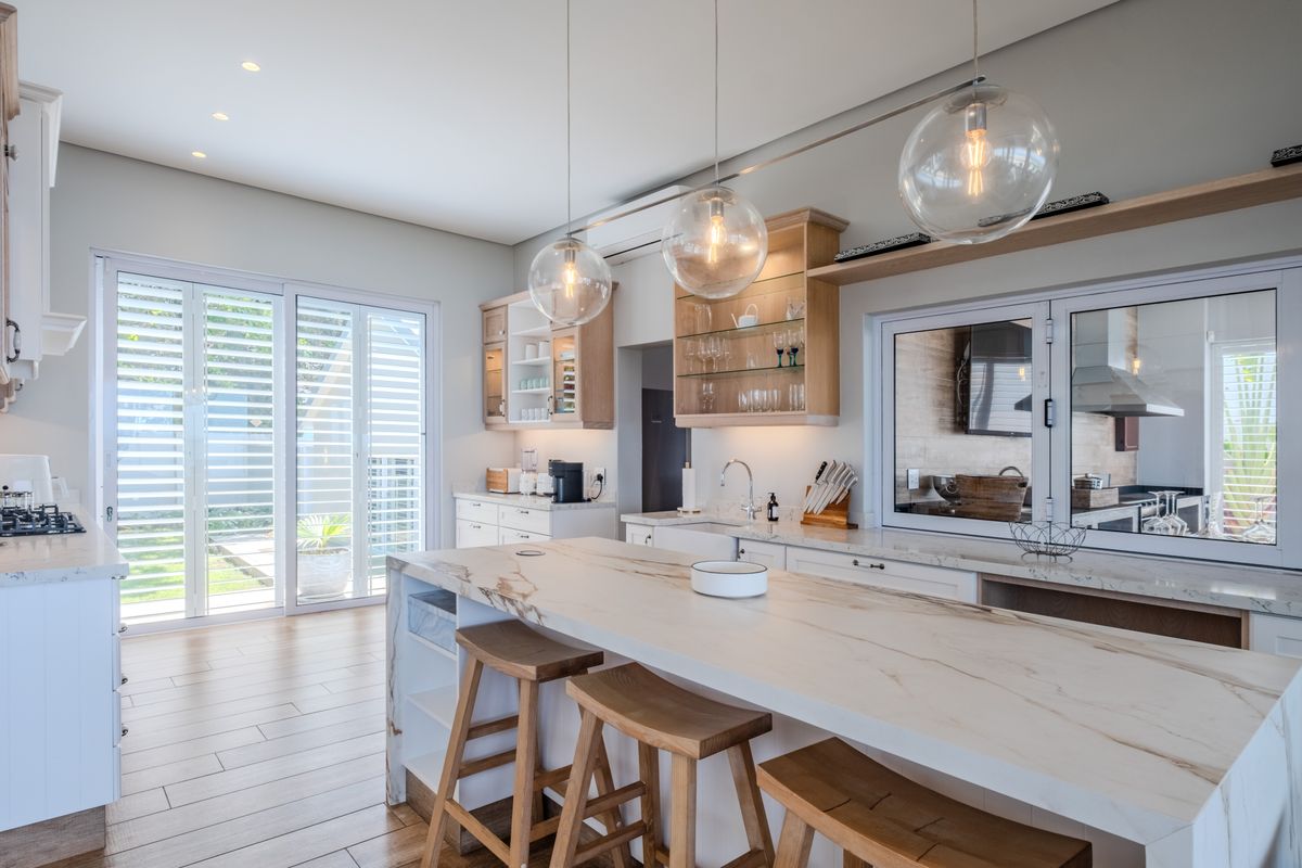 Modern kitchen featuring a large marble island, high-end cabinetry, gas cooktop, and seamless access to the outdoor area through sliding glass doors.