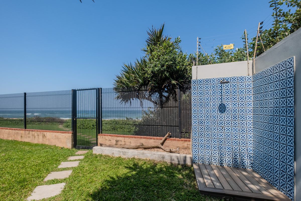 A private outdoor shower area featuring decorative blue and white tiles, timber decking, and direct access to the rear garden and coastal view.