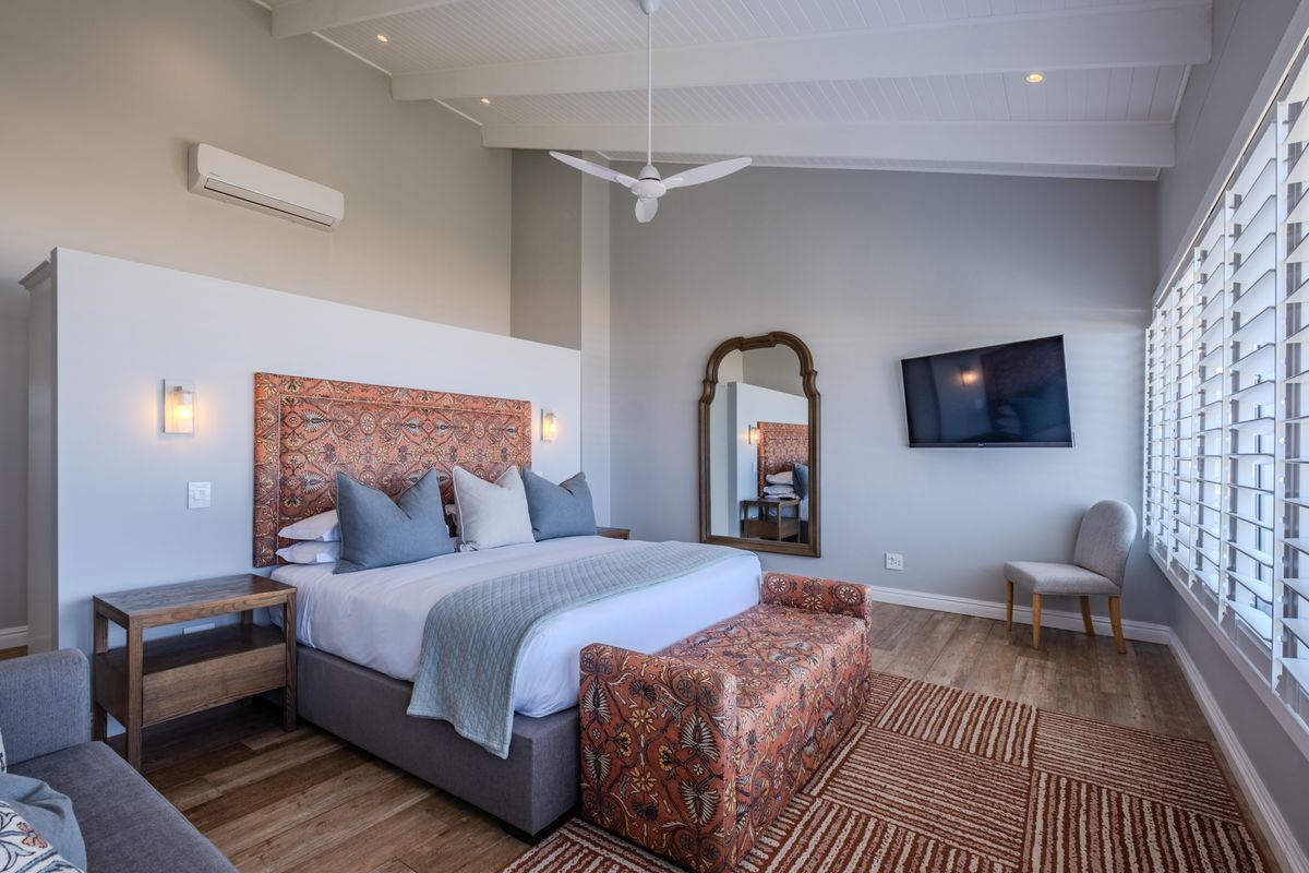 Spacious bedroom featuring a vaulted ceiling, ceiling fan, split-system air conditioning, and plantation shutters, finished with modern laminate flooring.
