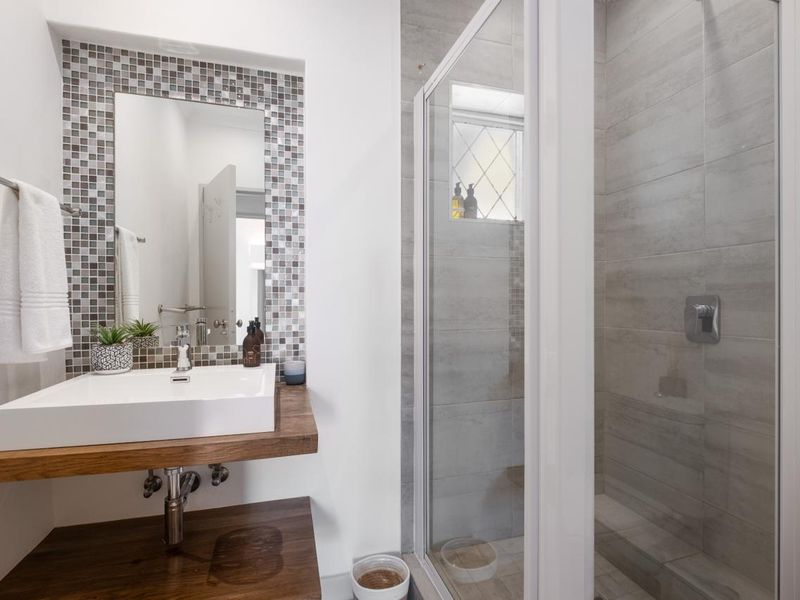 Modern bathroom featuring a vessel sink on a wooden vanity, mosaic tile accents, and a glass-enclosed shower with neutral wall tiling.