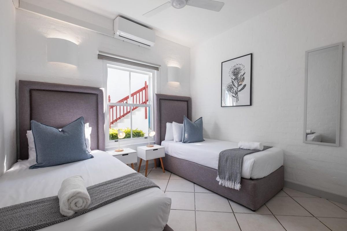A well-maintained bedroom featuring tiled flooring, a ceiling fan, and a split-system air conditioner, with natural light provided by a sash window.