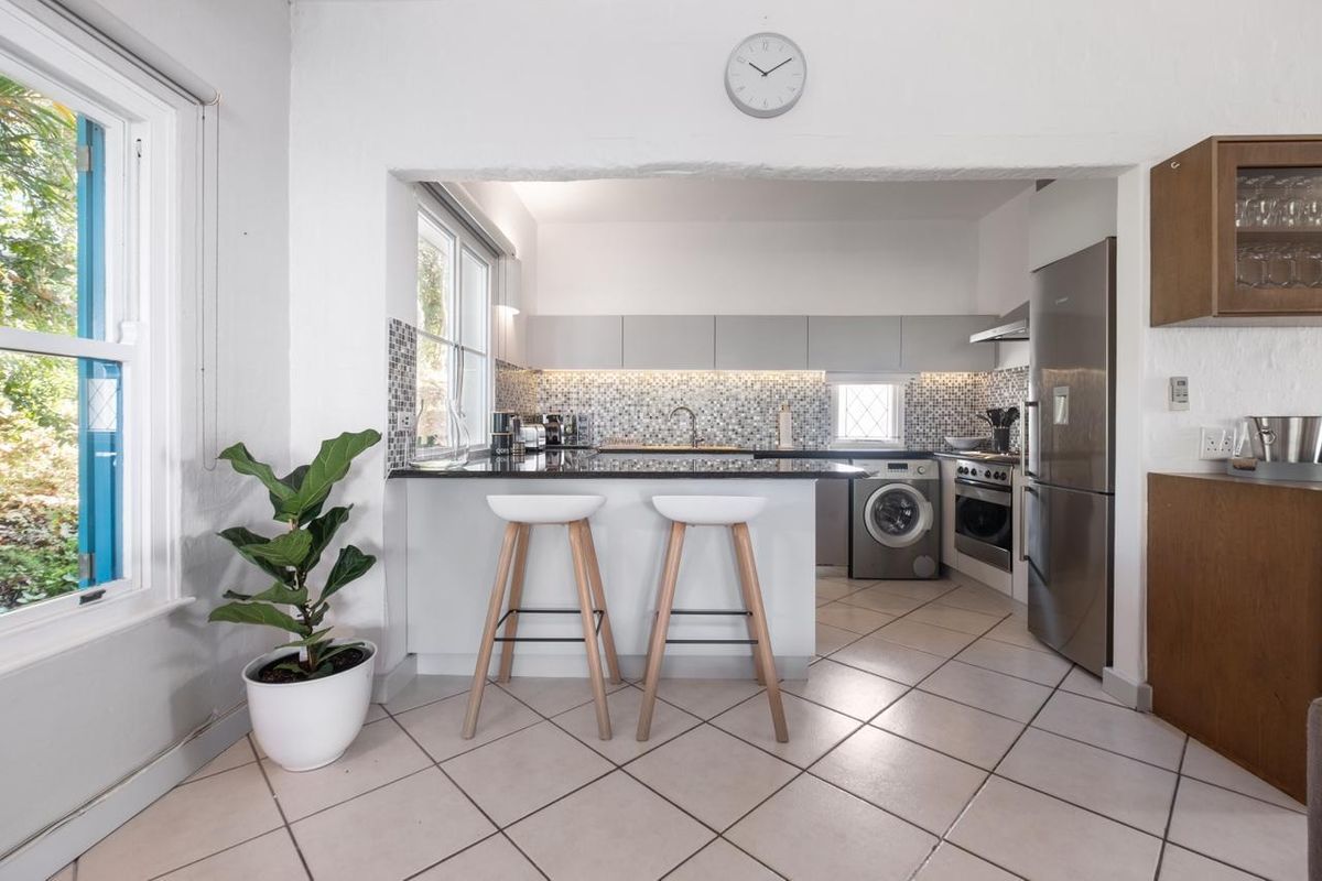A functional kitchen featuring modern grey cabinetry, mosaic tile backsplash, stone countertops, and integrated appliances, including a built-in oven and washing machine.