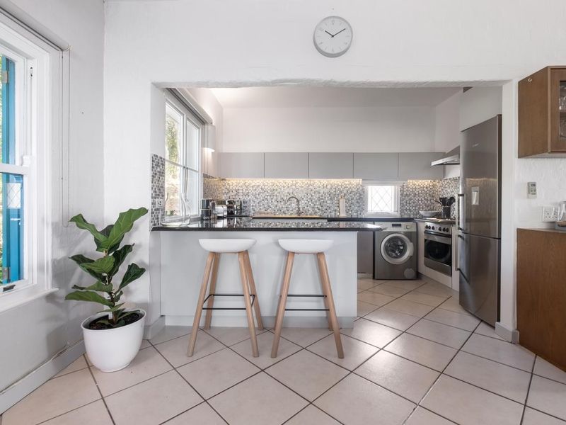 A functional kitchen featuring modern grey cabinetry, mosaic tile backsplash, stone countertops, and integrated appliances, including a built-in oven and washing machine.