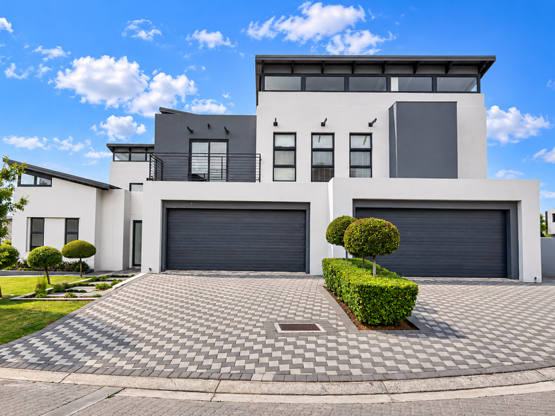 A modern, architecturally designed double-story home featuring a spacious paved driveway, double garage, and a clean, contemporary exterior finish.
