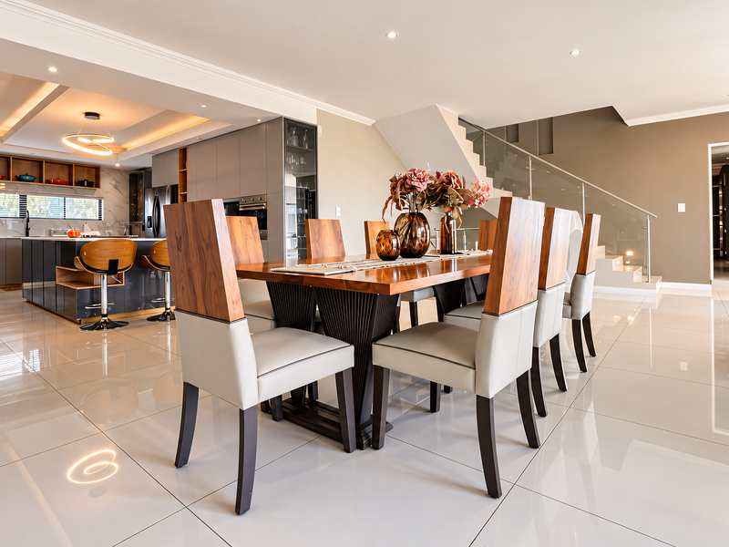 Spacious open-plan living and dining area featuring high-gloss floor tiles, modern kitchen cabinetry, and a contemporary staircase with a glass balustrade.