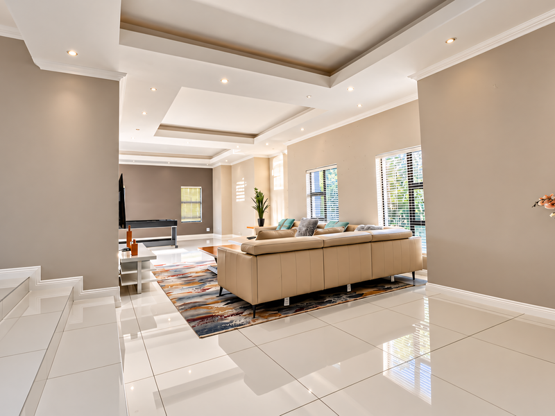 Spacious living area featuring high-gloss tiled flooring, a sophisticated recessed ceiling with integrated downlighting, and large windows fitted with venetian blinds.