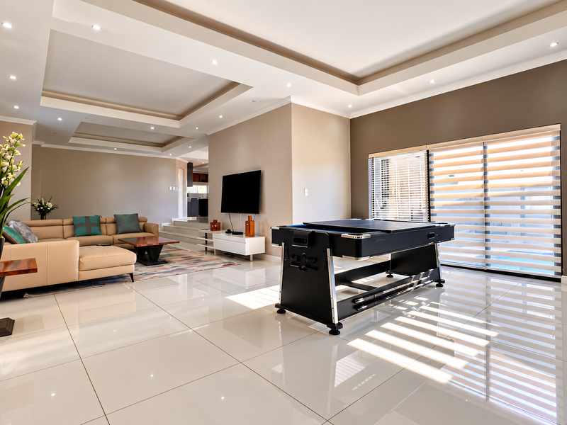 Spacious living area featuring a modern tray ceiling with recessed lighting, polished porcelain floor tiles, and large sliding glass doors with integrated blinds.