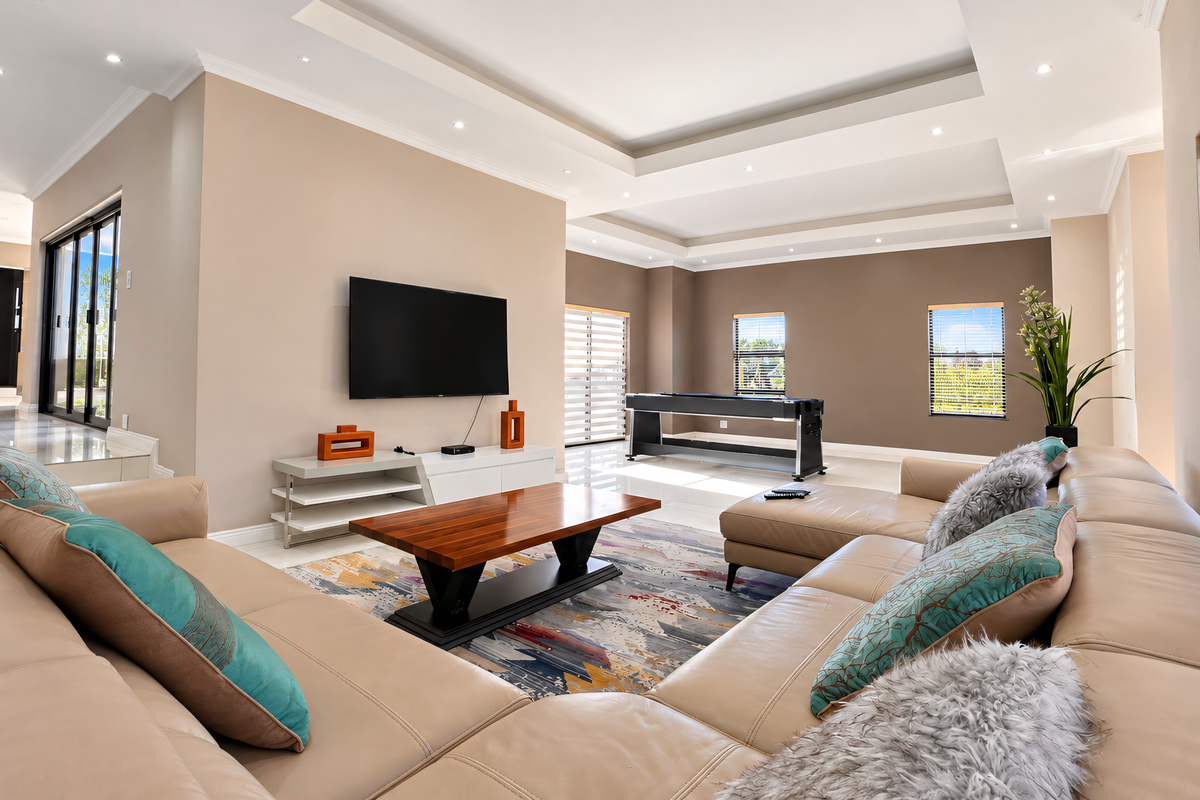 Spacious living room featuring a modern recessed ceiling with cove lighting, downlights, large sliding glass doors, and neutral tiled flooring.