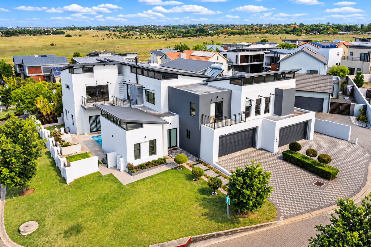Aerial view of a modern multi-level residential property featuring a double garage, swimming pool, solar panels, and landscaped garden in a suburban estate.