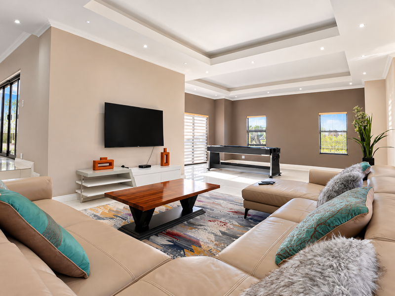 Spacious living room featuring a modern recessed ceiling with cove lighting, downlights, large sliding glass doors, and neutral tiled flooring.