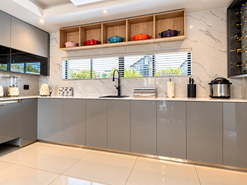 Modern kitchen featuring high-gloss grey cabinetry, marble-look splashback, integrated wine storage, and open timber shelving with sleek contemporary finishes.
