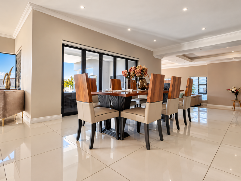 Spacious open-plan living and dining area featuring polished porcelain floor tiles, recessed ceiling lighting, crown molding, and large sliding glass doors leading outdoors.