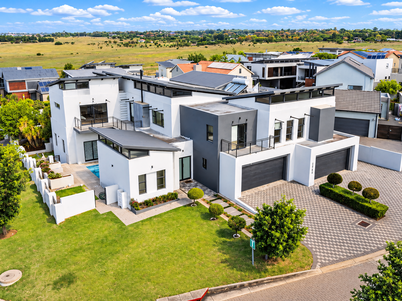 Aerial view of a modern multi-level residential property featuring a double garage, swimming pool, solar panels, and landscaped garden in a suburban estate.