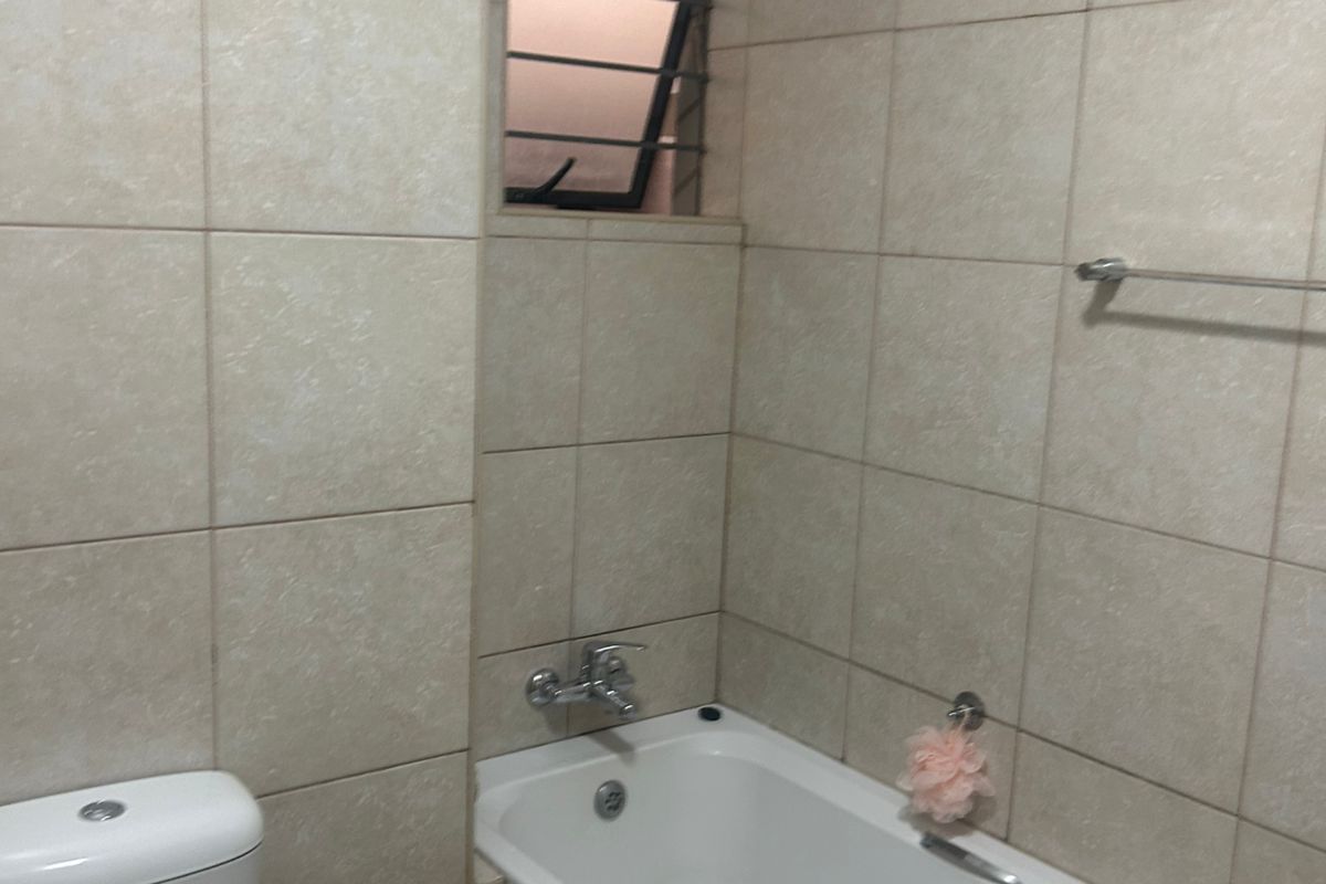 A functional bathroom featuring full-height wall tiling, a standard bathtub with chrome mixer tap, and a white ceramic toilet.