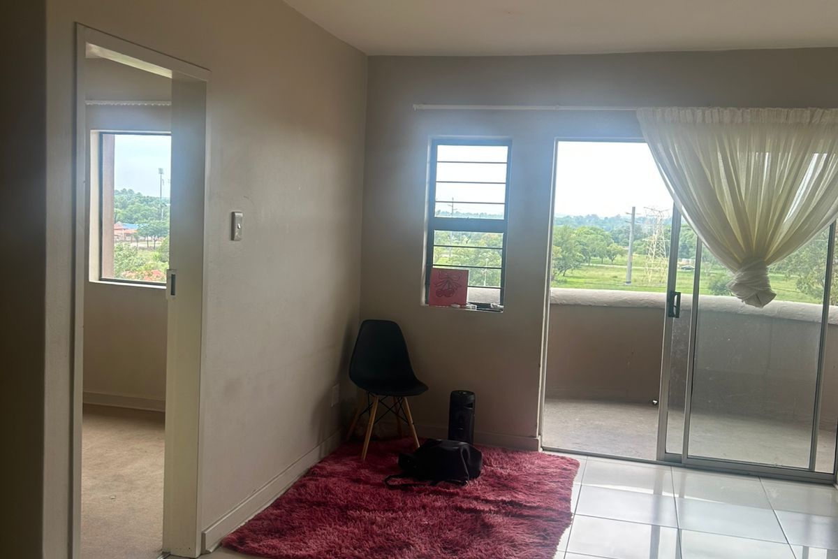 A bright living area featuring tiled flooring, large sliding glass doors leading to a balcony, and an adjacent room with carpeted flooring.