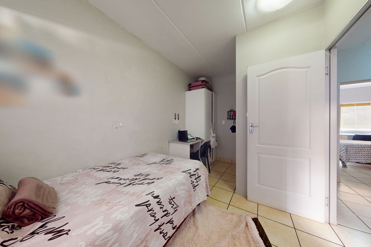A functional bedroom featuring tiled flooring and a standard interior door, with a view into an adjacent room.