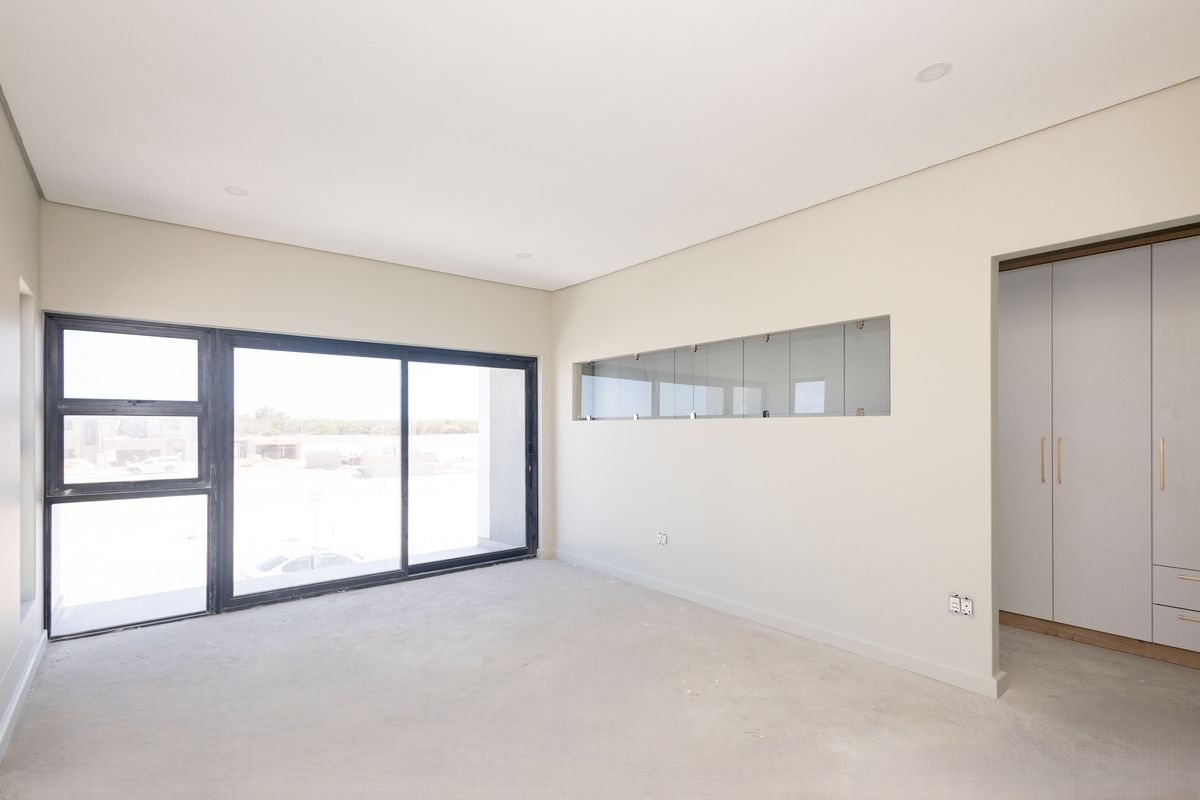 A bright, empty bedroom featuring modern built-in cupboards, a large sliding glass door, and a unique horizontal feature window, awaiting final flooring installation.