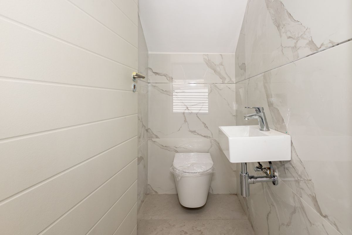A modern, compact guest bathroom featuring marble-effect wall tiling, a wall-mounted basin with chrome fixtures, and a wall-mounted toilet.