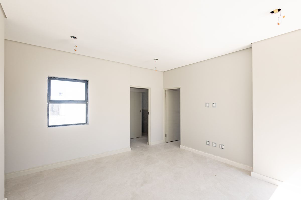 A bright, empty bedroom featuring neutral walls, tiled flooring, and modern aluminium window frames, currently awaiting final light fixture installation.