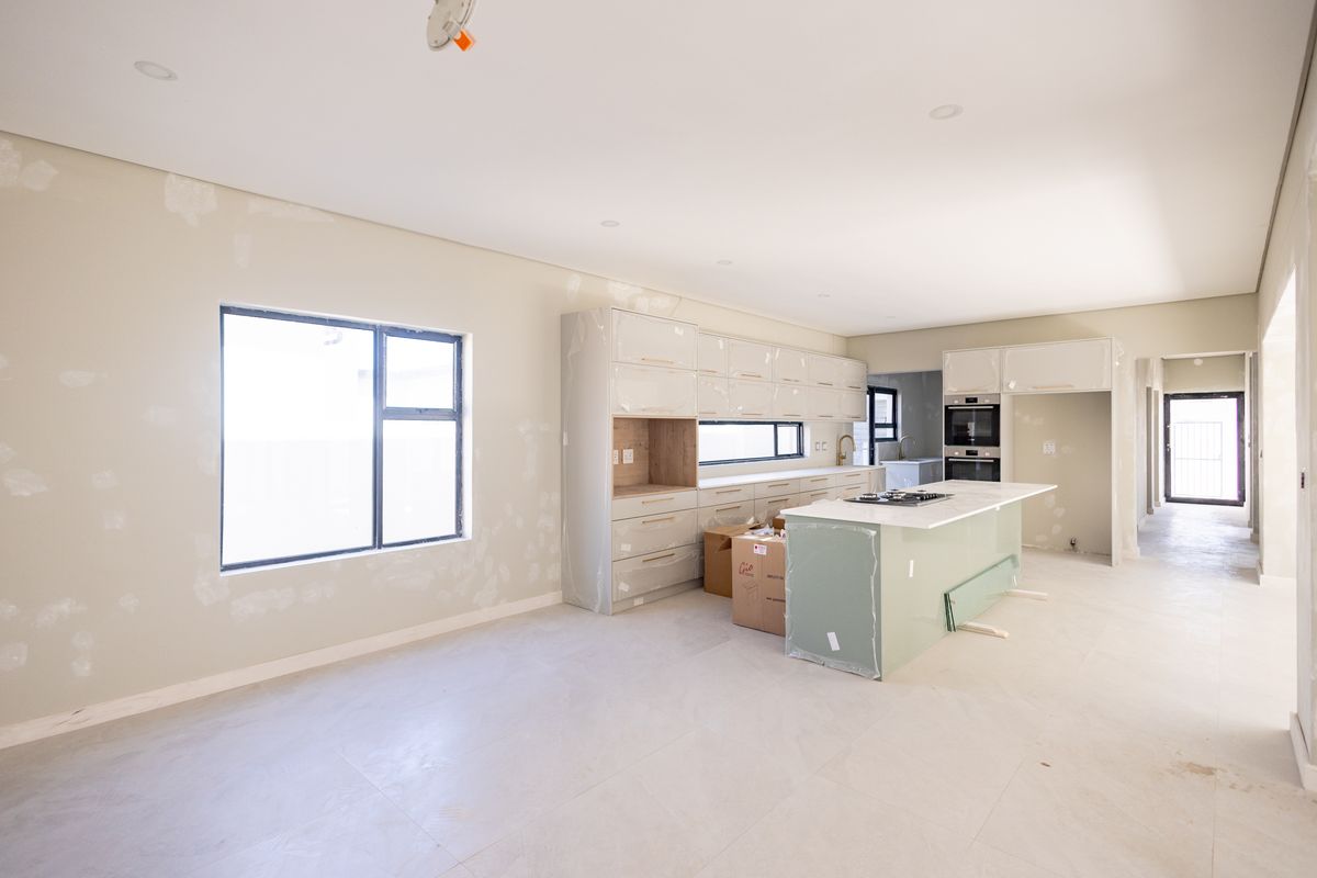 An unfinished kitchen space featuring modern cabinetry, a central island with a gas hob, and built-in oven, currently awaiting final wall finishes and completion.