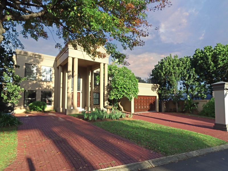 A grand double-story residence featuring a prominent portico entrance, brick-paved driveway, and an integrated double garage set within a well-maintained landscaped garden.