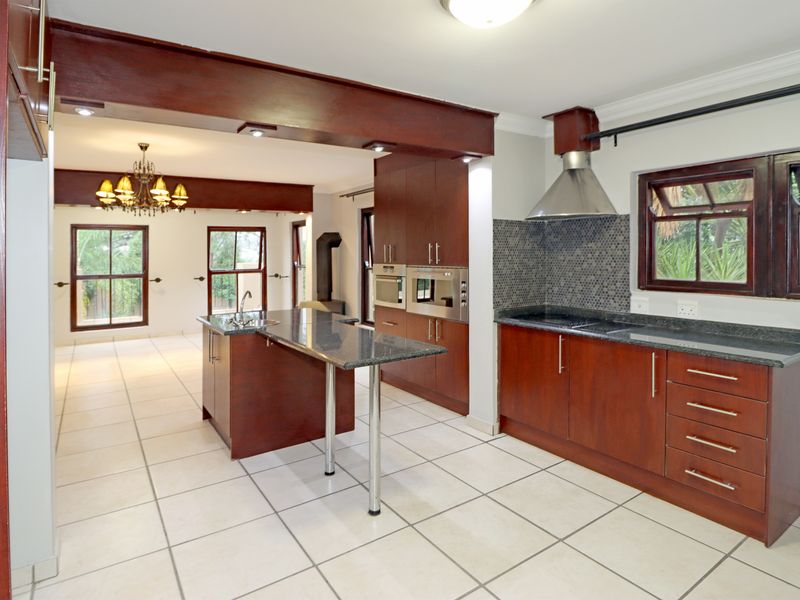 Spacious open-plan kitchen featuring dark wood cabinetry, granite countertops, built-in appliances, and a central island, seamlessly flowing into the adjacent living area.