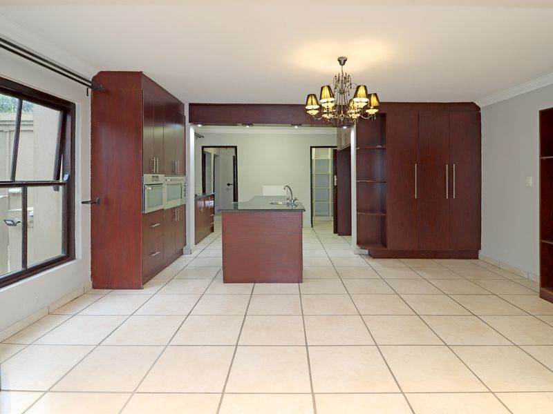 Spacious kitchen featuring dark wood cabinetry, a central island with a sink, double wall ovens, and neutral tiled flooring.