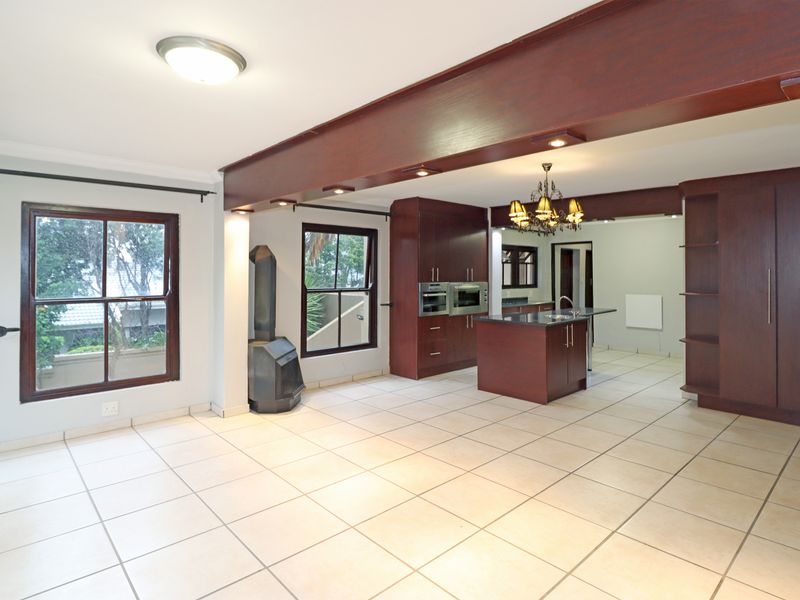 Spacious open-plan living and kitchen area featuring dark wood cabinetry, a central island, tiled floors, and a built-in fireplace.